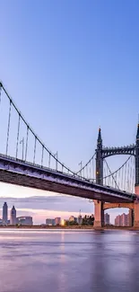 Beautiful suspension bridge at sunset with city skyline in background.