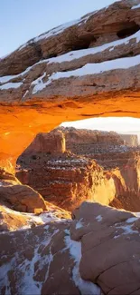 Sunset over snow-capped canyon with natural arch.