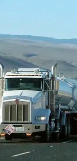 Silver tanker truck on open highway under clear sky.