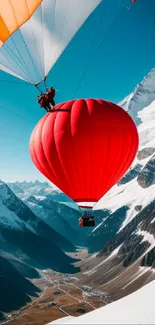 Red hot air balloon over snowy mountains at sunrise.