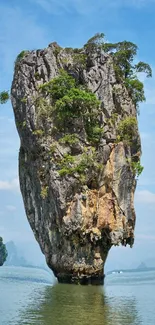 Towering rock island in serene blue ocean under a clear sky, lush with greenery.