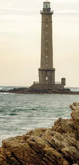 A tall lighthouse stands by the rocky sea shore under a beige sky.