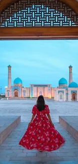 Woman in red dress admiring mosque through ornate doors.