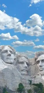 Mount Rushmore under a bright blue sky with scattered clouds.