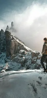 A lone hiker stands on a snowy mountain with a breathtaking view of peaks and mist.