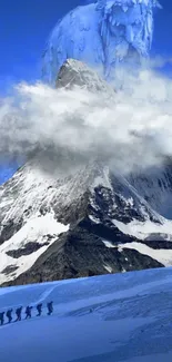 Hikers ascend a snow-covered mountain beneath a clear blue sky with clouds.