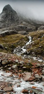 Majestic mountain landscape with a misty peak and flowing stream.