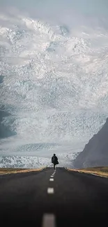 A lone traveler on a road leading to majestic snowy mountains.