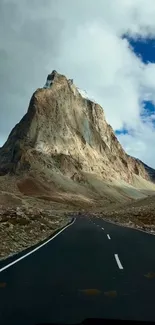 A winding road leading to a majestic mountain under a partly cloudy sky.