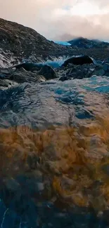 A serene mountain stream flowing over rocks under a cloudy sky.