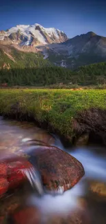 Majestic mountains with a flowing stream and lush greenery under a clear sky.