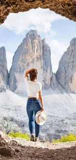 Person stands in cave, viewing majestic mountains.