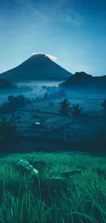 Mountain at night with blue sky and green grass in foreground.