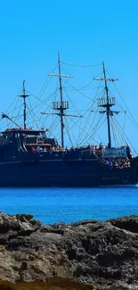 A pirate ship sails across the vibrant blue ocean with a clear sky backdrop.