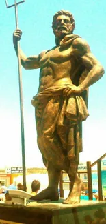 Poseidon statue with a trident against a blue sky.