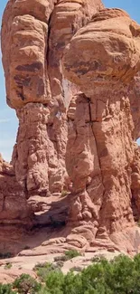 Majestic red rock formation under a clear blue sky with green foliage.