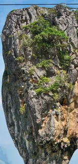 Majestic rocky cliff with greenery under a blue sky.