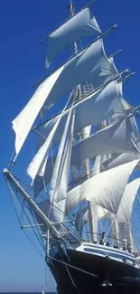 Majestic sailing ship with white sails under a clear blue sky.