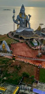 Majestic statue of Shiva at sunset over the ocean with vibrant colors.