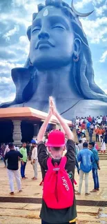 Person praying before large Shiva statue outdoor scene.