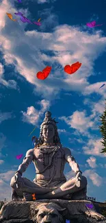 Serene statue of Shiva under a vibrant blue sky with scattered clouds.