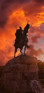 Silhouette of an equestrian statue against a vibrant orange sunset sky.