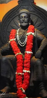 A black statue with a vibrant red garland on a decorative throne.