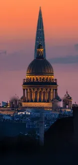 Cityscape with dome and spire at sunset in deep orange hues.