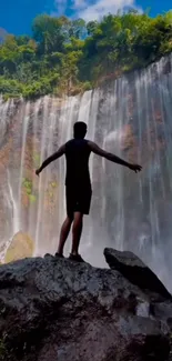 Silhouette person stands by a majestic waterfall.