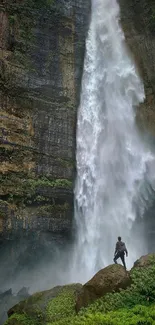 Man standing by a majestic waterfall amidst lush greenery and rocky cliffs.
