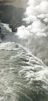 Majestic waterfall with misty clouds cascading down rocky cliffs.