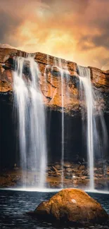 Majestic waterfall at sunset with glowing orange sky.