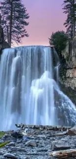 Serene waterfall cascading under a pink sky with surrounding green trees.