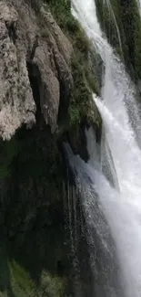 Majestic waterfall cascading over rocky cliff in lush green scenery.