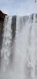 Majestic waterfall cascades down rocky cliffs in a serene nature scene.