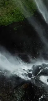 Majestic waterfall over dark rocks with lush greenery background.