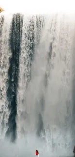 Majestic waterfall cascading down a cliff with a person in a red coat standing nearby.