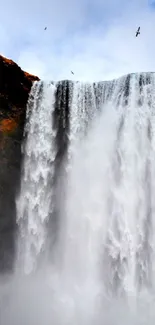 Majestic waterfall with birds above and rocky cliffs, perfect for mobile wallpaper.