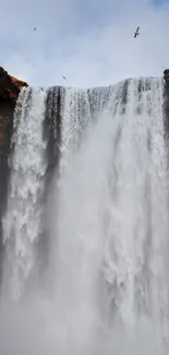 Waterfall with cliffs and a blue sky, person in red coat at the bottom.