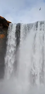 Majestic waterfall cascading down cliffs with a lone figure in a vibrant jacket.