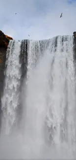 Majestic waterfall with a lone figure in a vibrant jacket standing at the base.