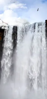 Cascading waterfall with surrounding cliffs and blue sky.