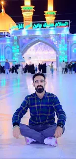 Man sitting in front of illuminated mosque at night.