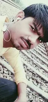 Man in yellow shirt sitting on railway tracks.