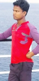 Man in red shirt standing by the ocean on a sunny day.