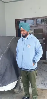 Man in blue hoodie standing beside covered car.