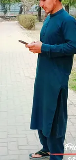 A man in a blue kurta checks his phone outside.