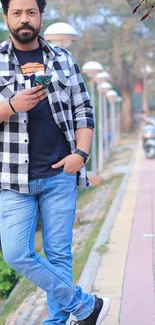 Man in jeans and plaid shirt with smartphone, urban setting.