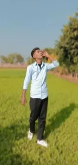 Man walking in a green field beneath a blue sky.