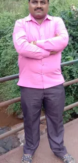 Man in a pink shirt standing on a bridge with greenery.